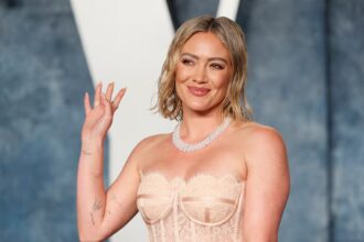 Hilary Duff κρατά μικρόφωνο στη σκηνή χαμογελώντας στο κοινό