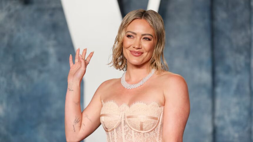 Hilary Duff κρατά μικρόφωνο στη σκηνή χαμογελώντας στο κοινό