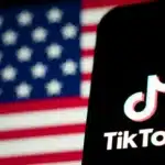 Χρήστης του TikTok χαμογελά κρατώντας κινητό με φόντο τη σημαία των ΗΠΑ