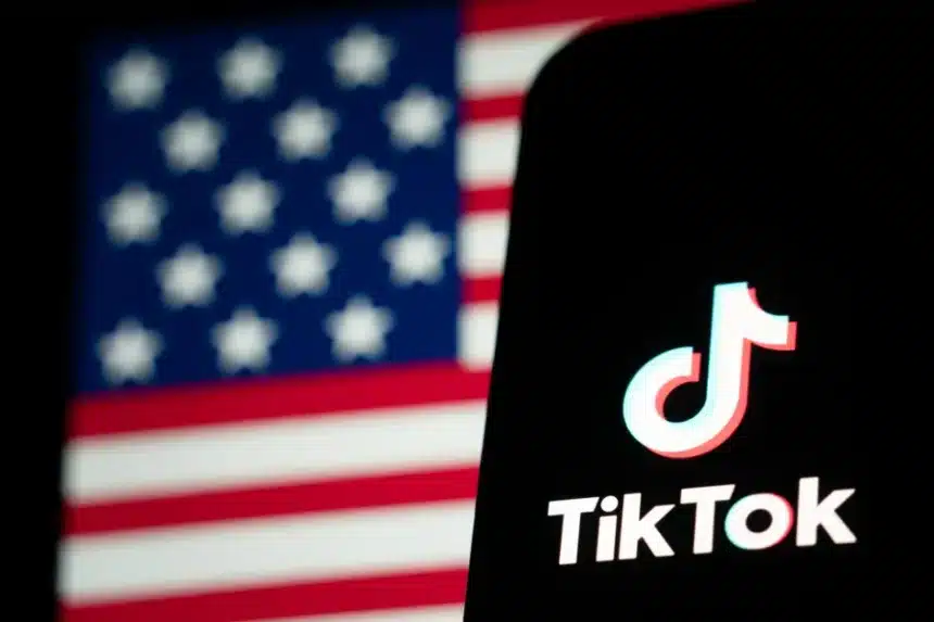 Χρήστης του TikTok χαμογελά κρατώντας κινητό με φόντο τη σημαία των ΗΠΑ