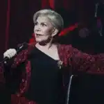 Μαρινέλλα σε εμβληματική εμφάνιση με φόντο σκηνή και φώτα, αναφορά στη διαχρονική καριέρα της