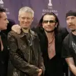 U2 σε σκοτεινή σκηνή με δραματικό φωτισμό εμπνευσμένο από το Easter Lily και έντονη συναισθηματική ατμόσφαιρα